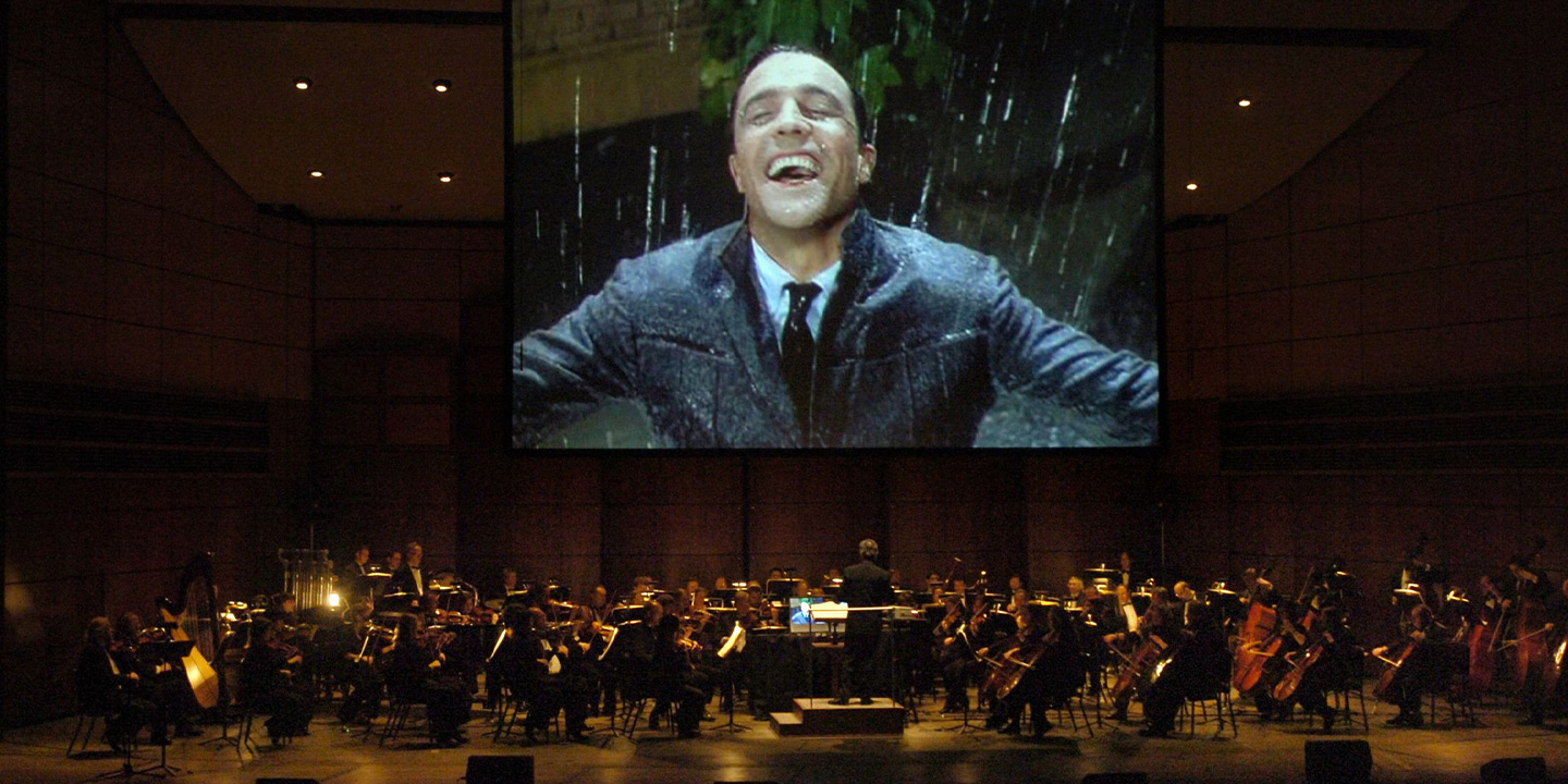 A stage featuring an orchestra and a large screen showing the movie Singin in the Rain